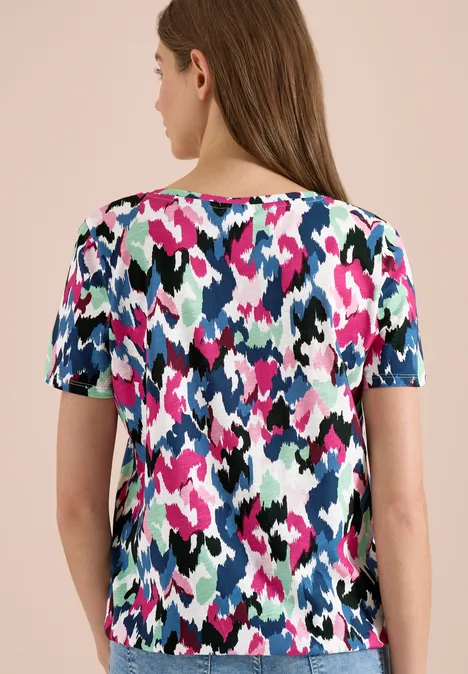 Vrouw van achteren in een T-shirt met korte mouwen en abstract patroon in roze, blauw, wit, zwart en groen.