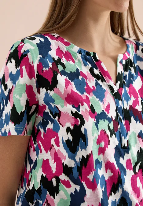 Damesblouse met korte mouwen en abstract, meerkleurig patroon in roze, blauw, zwart en wit.