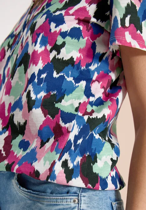 Persoon draagt een T-shirt met korte mouwen, kleurrijk abstract dessin en een spijkerbroek.