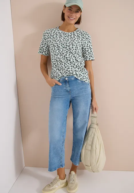 Persoon in een T-shirt met patroon, rechte blauwe jeans, witte sneakers en een tas.