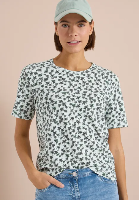 Een persoon draagt een wit T-shirt met een groen bloemenpatroon, korte mouwen, casual stijl.