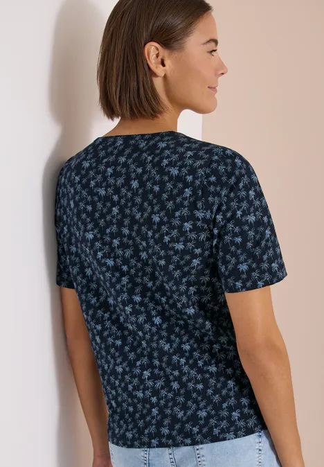 Persoon van achteren met kort bruin haar, draagt een zwarte T-shirt met blauw bloemenpatroon.