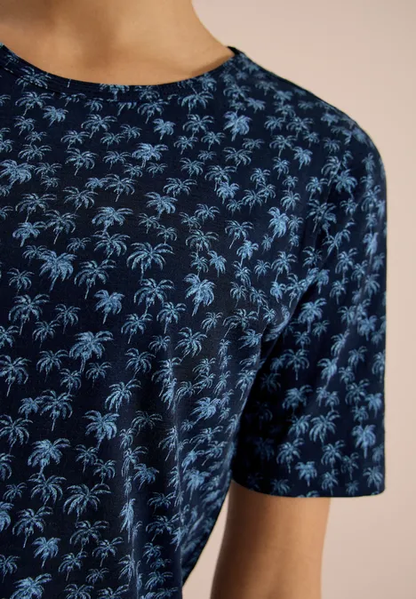 Close-up van een donkerblauw T-shirt met een lichtblauw all-over palmboomprint.