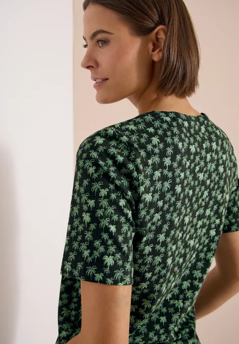 Achteraanzicht van een persoon met kort haar en een groen T-shirt met bloemenmotief.