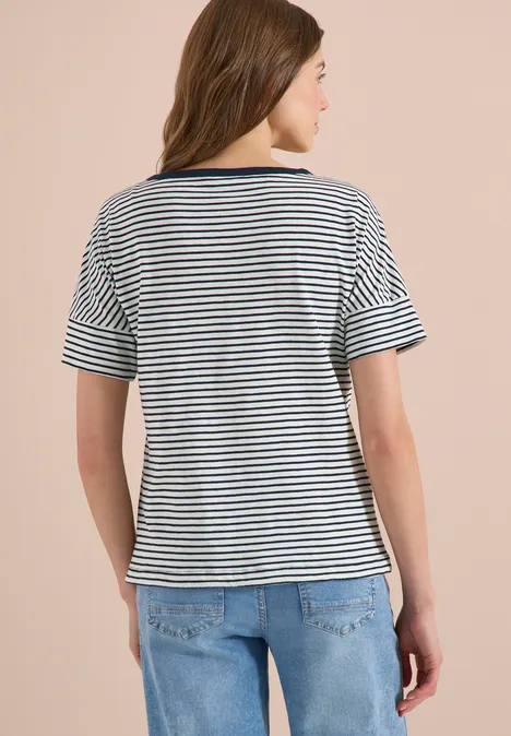 Rückansicht einer Frau in blau-weiß gestreiftem T-Shirt und Jeans vor hellem Hintergrund.