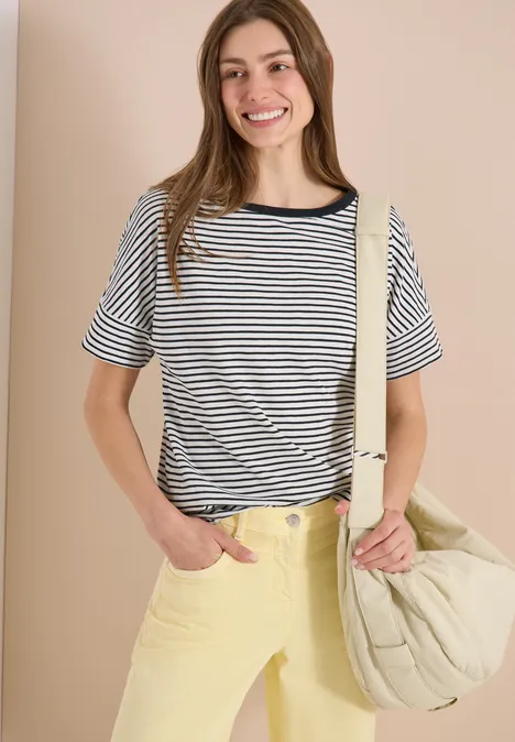 Vrouw in gestreept shirt, brede gele broek en grote beige gewatteerde tas.