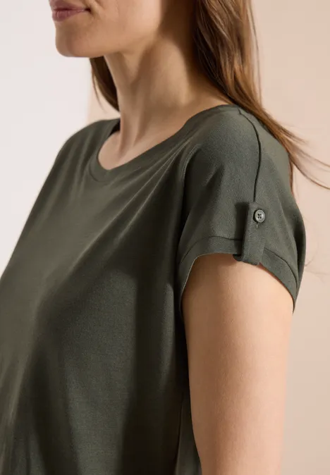 Frau im Profil trägt ein kurzärmeliges, olivgrünes T-Shirt mit aufgekrempelten Ärmeln.