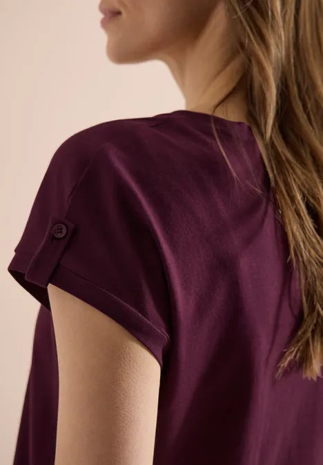 Damen-T-Shirt in dunklem Violett mit hochgekrempeltem Ärmel und Knopfdetail, seitliche Rückansicht.