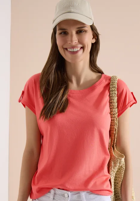 Person mit rotem T-Shirt, Cap und Stroh-Tasche, Gesicht unkenntlich gemacht