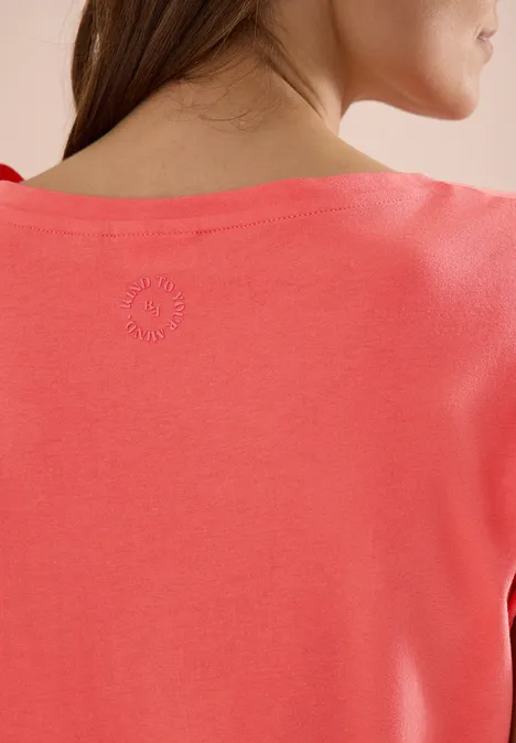 Rückenansicht einer Frau im korallenfarbenen T-Shirt, leicht seitlich gewandt