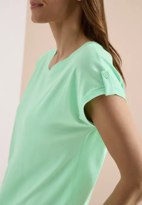 Eine Frau im Profil in einem mintgrünen T-Shirt mit kurzen Ärmeln.