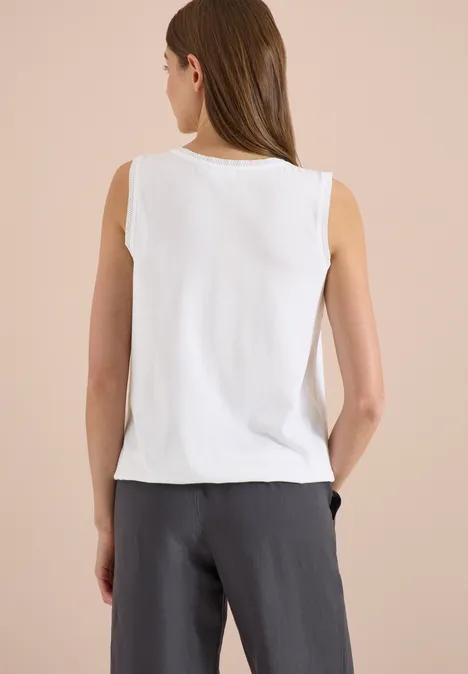 Vrouw van achteren in een wit mouwloos top en een grijze broek.