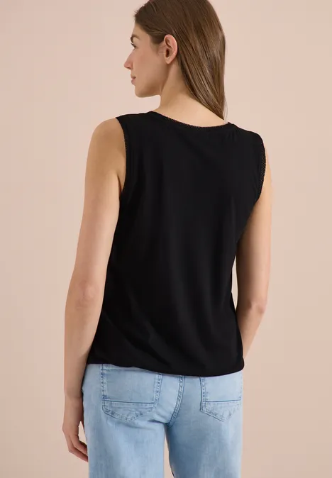 Femme de dos portant un débardeur noir et un jean bleu clair sur un fond neutre.