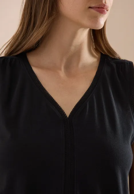 Gros plan sur une femme en haut noir à encolure en V, montrant son cou, ses épaules et une partie du visage.