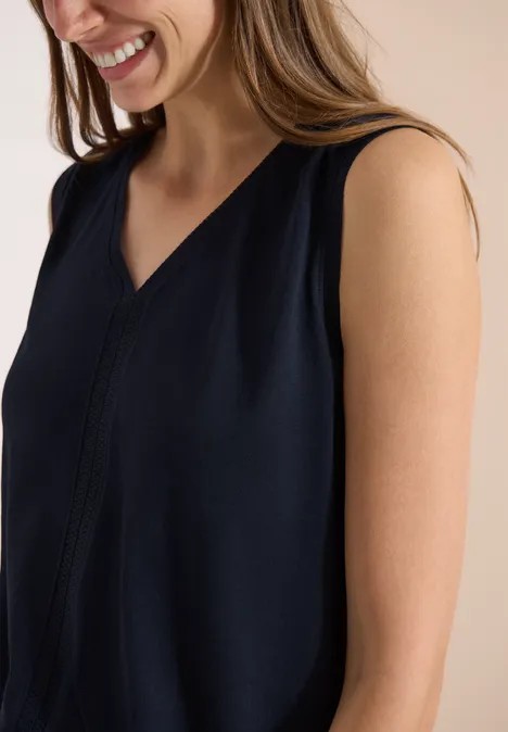 Een lachende vrouw draagt een mouwloos donkerblauw topje met V-hals.