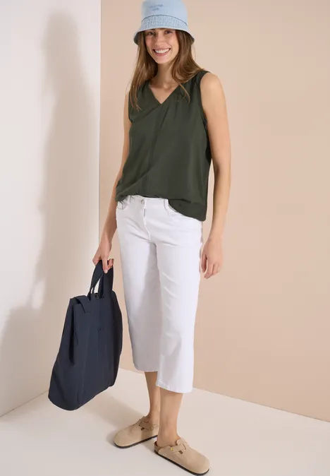 Frau trägt dunkelgrünes Top, weiße Culotte, beige Loafer und navy Tasche.