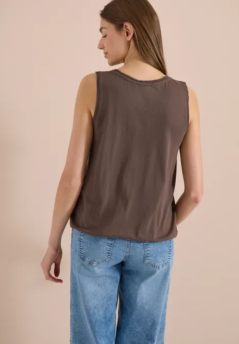 Frau von hinten in ärmellosem braunem Top und weiten, hellblauen Jeans.