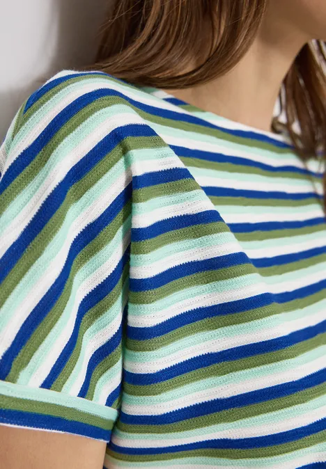 Frau trägt ein gestreiftes, kurzärmliges Oberteil in Grün, Blau und Weiß.