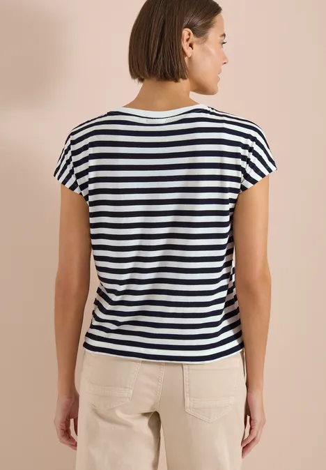 Een vrouw van achteren draagt een zwart-wit gestreept T-shirt met korte mouwen en een lichte broek.