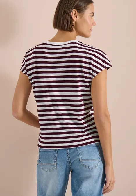 Frau steht Rücken zur Kamera und trägt gestreiftes T-Shirt und blaue Jeans.