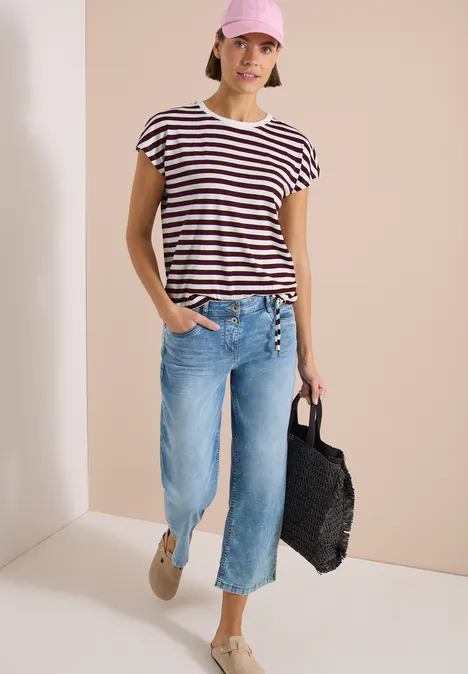 Frau in gestreiftem T-Shirt, hellblauer Culotte-Jeans, beigen Schuhen und schwarzer Tasche