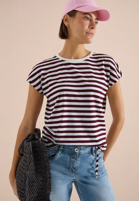 Frau in kurzärmeligem weiß-dunkel gestreiftem T-Shirt, hellblauen Jeans, Stricktasche und Cap.