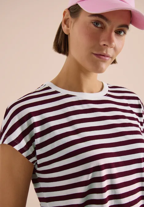 Oberkörper einer Person in weiß-bordeaux gestreiftem T-Shirt, neutraler Hintergrund.