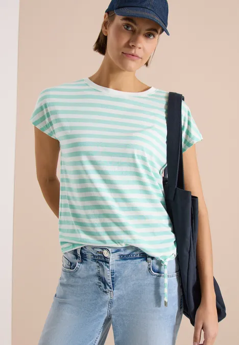 Person in mint-weiß gestreiftem T-Shirt, blauer Jeans, mit dunkelblauer Tasche und Cap.