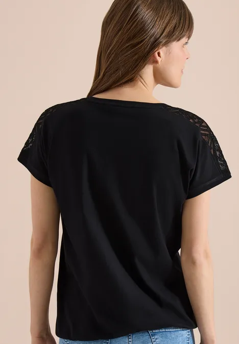 Frau von hinten trägt schwarzes T-Shirt mit kurzen Ärmeln und Spitzenapplikationen an den Schultern.