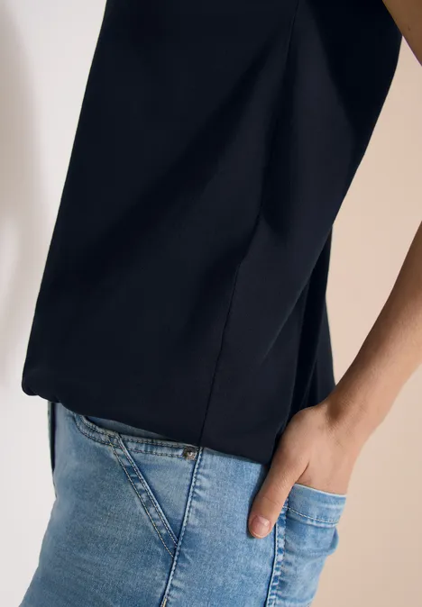 Person trägt schwarzen Oberteil und helle Jeans, rechte Hand in Tasche