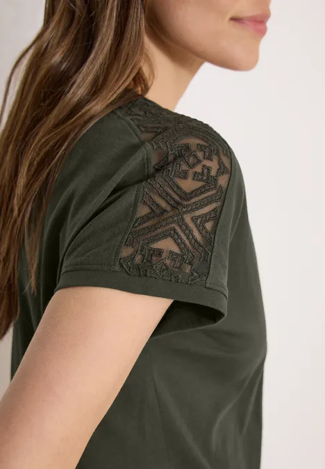 Olivegrünes T-Shirt mit geometrischem Spitzen-Einsatz auf der Schulter an einer Frau.