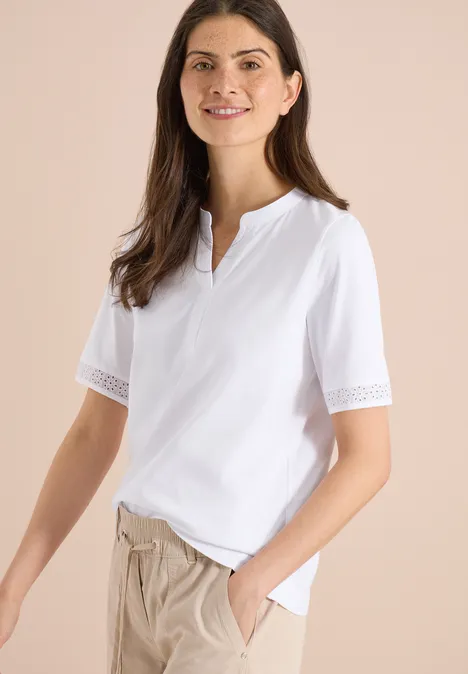 Vrouw draagt wit shirt met kanten korte mouwen en een beige broek.