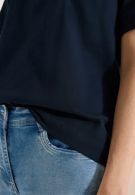 Een persoon draagt een donkerblauw T-shirt en een lichtblauwe spijkerbroek, alleen de torso is zichtbaar.