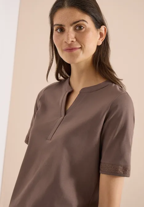 Vrouw draagt een eenvoudig bruin topje met korte mouwen, V-hals en kanten randjes