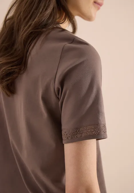 Zijaanzicht van een vrouw in een bruin T-shirt met korte mouwen en een sierlijke zoom.