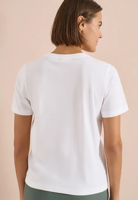 Rückansicht einer Person mit kurzem Bob, die ein schlichtes weißes T-Shirt vor neutralem Hintergrund trägt.