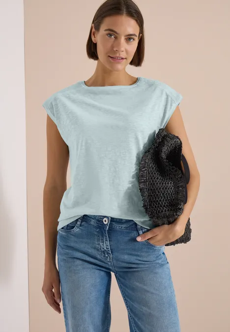 T-Shirt aus Jersey im Garment Dye Look crystal mint Frau trägt hellblaues ärmelloses Oberteil, blaue Jeans und hält schwarze Tasche.
