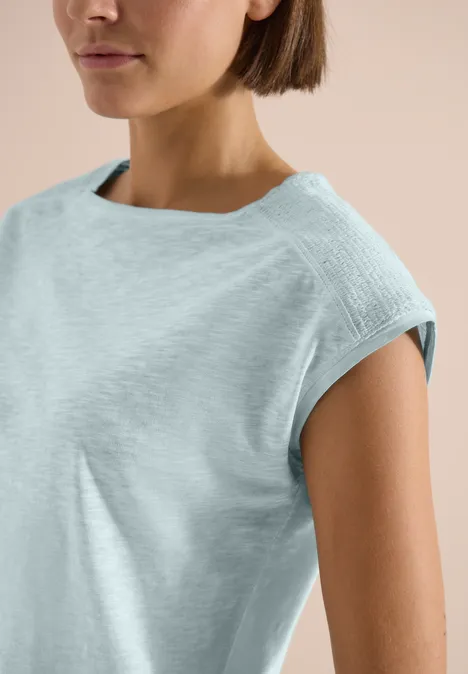 T-Shirt aus Jersey im Garment Dye Look crystal mint Nahe Einstellung einer Frau in einem hellblauen, ärmellosen Oberteil vor neutralem Hintergrund.