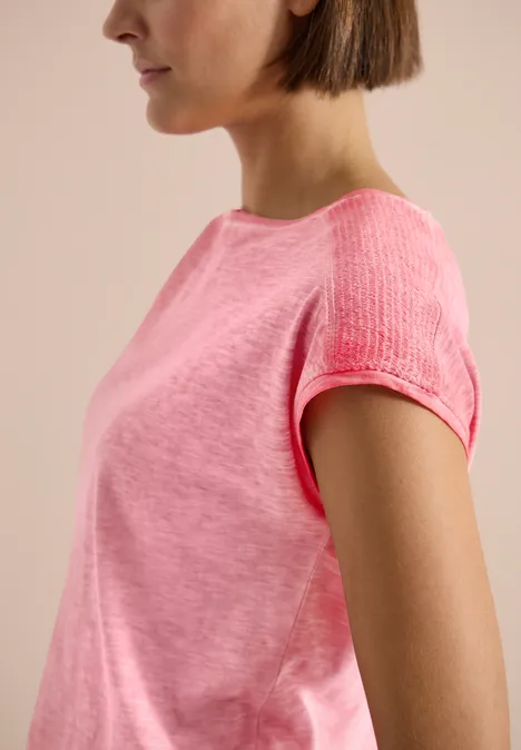 T-Shirt aus Jersey im Garment Dye Look coral Seitliches Profil einer Person in einem pinkfarbenen kurzärmligen T-Shirt vor neutralem Hintergrund.