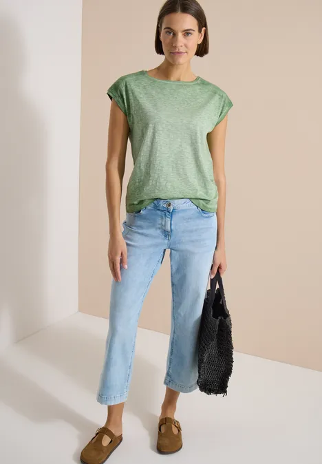 Vrouw met groen T-shirt, lichte rechte jeans, bruine suède loafers en zwarte net-tas.