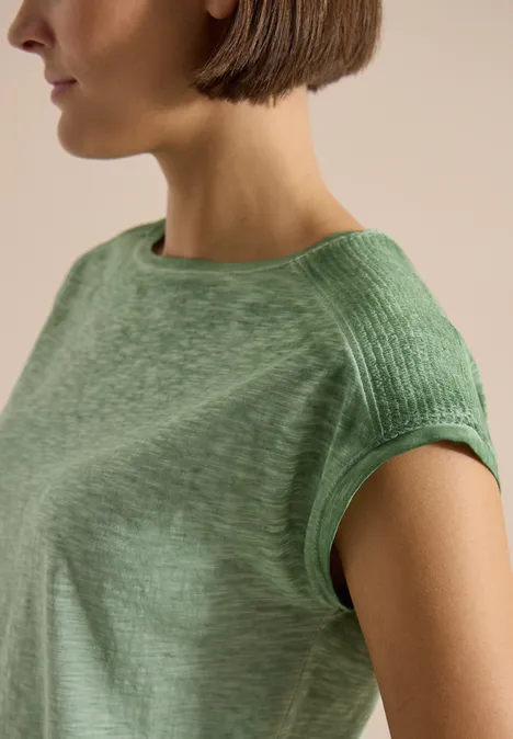 Vrouw met korte bob draagt een lichtgroen kort T-shirt in een close-up.