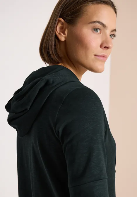 Seitliche Aufnahme einer Person in schwarzem Kapuzenpullover vor neutralem Hintergrund.