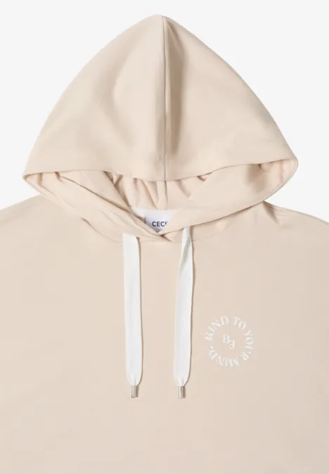 Hellbeiger Kapuzenpullover mit weißen Kordeln und kleinem weißen Schriftzug auf der Brust.