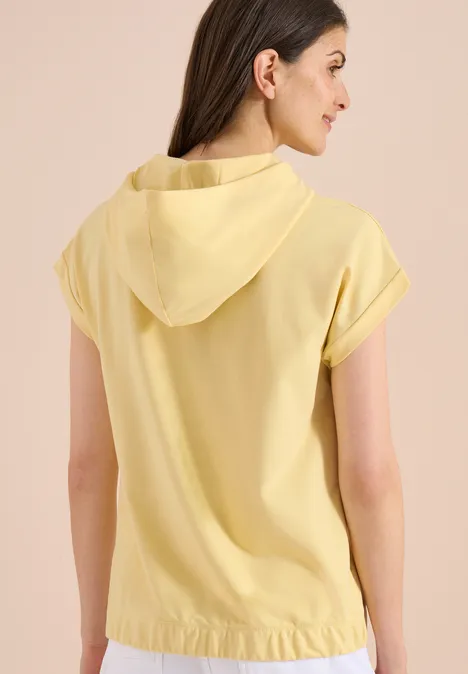 Frau von hinten in hellgelbem, kurzärmeligem Kapuzenoberteil.