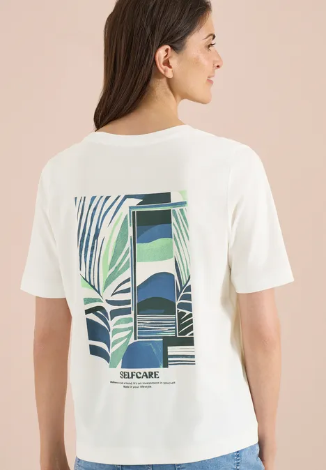 Vrouw van achteren in wit shirt met abstract groen-blauw patroon en ‘SELFCARE’ opdruk.