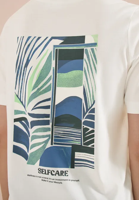 Wit T-shirt met groen-blauw bladmotief en abstracte poort, tekst SELFCARE