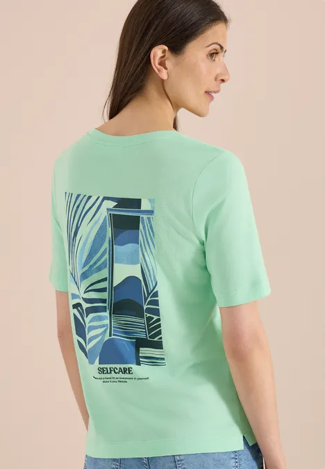Vrouw van achteren in mintgroen T-shirt met abstract landschapsgrafiek op de rug