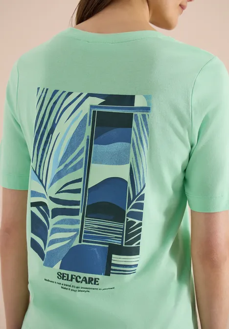 Persoon van achteren in mintgroen T-shirt met abstract blauw motief en tekst 'SELFCARE'.