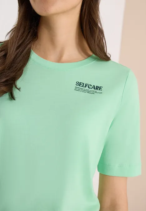 Close-up van een mintgroen T-shirt met de tekst 'SELFCARE' op de borst
