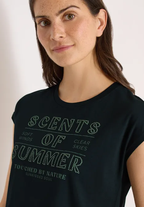 Een vrouw in een zwart t-shirt met groene opdruk 'Scents of Summer'.